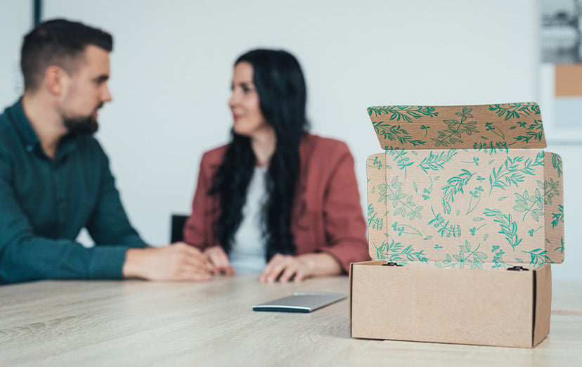 Zwei Personen betrachten eine nachhaltige Kartonverpackung mit Pflanzenmotiv